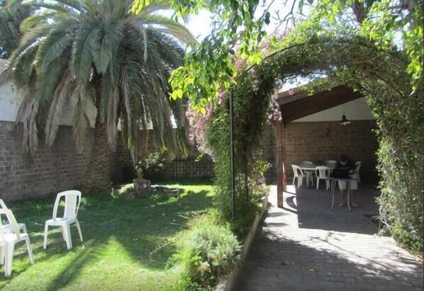 A covered patio area with a brick wall, a palm tree, and a table with chairs. - Paraná Hostel (Parana)