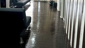 Un hall d’entrée spacieux avec un plancher en bois foncé, un canapé gris agrémenté de coussins et un téléviseur fixé au mur.