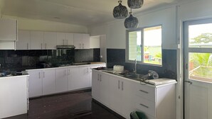 Une cuisine avec des meubles blancs, un plan de travail noir et une fenêtre donnant sur un espace verdoyant.