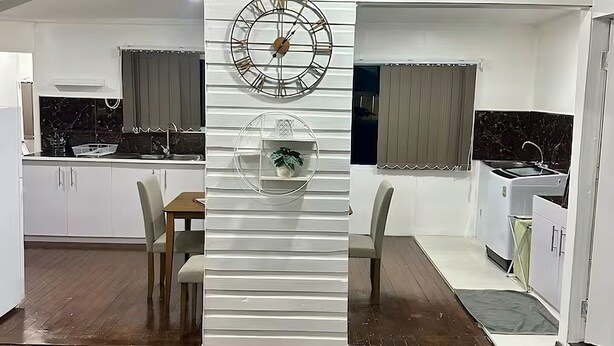 Une cuisine compacte dotée d’un climatiseur intégré, d’une horloge décorative et d’un petit coin repas avec une table et des chaises.