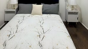 Une chambre à coucher comprenant un lit, deux tables de chevet, un ventilateur de plafond et une œuvre d’art accrochée au mur.