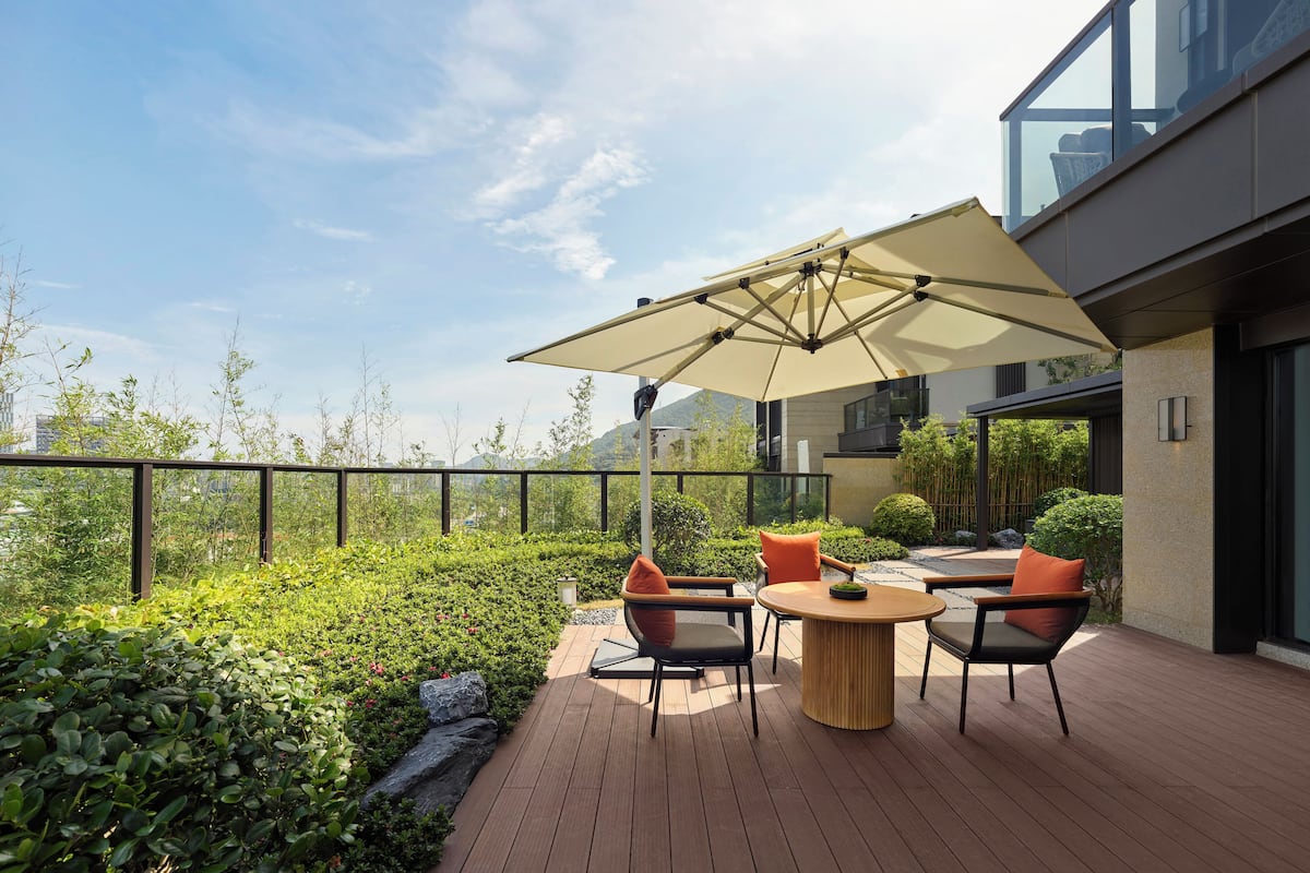 A modern outdoor patio with a round wooden table and chairs, an umbrella, and a view of the cityscape.