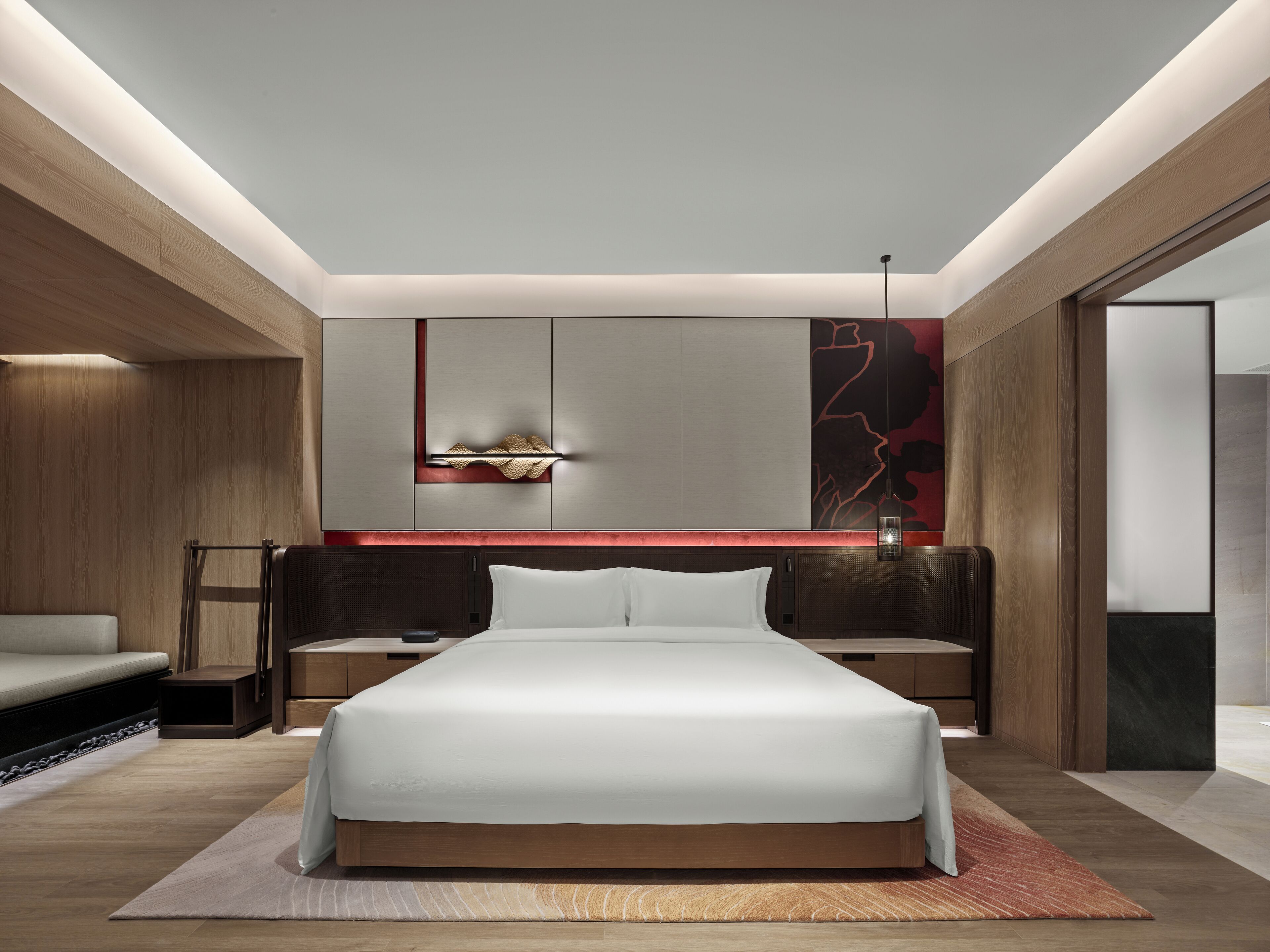 A modern bedroom with a large bed, wooden paneling, and a red accent wall.