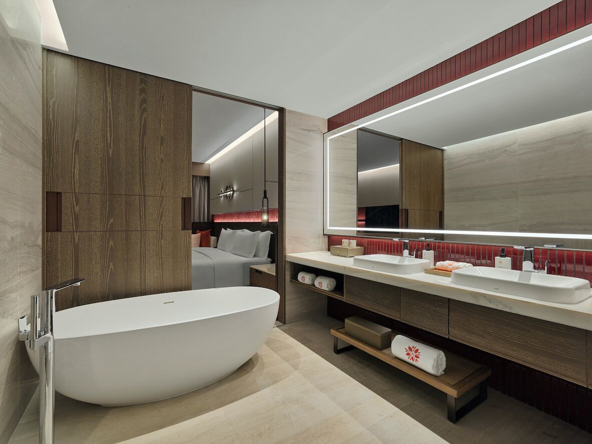 Ein modernes Badezimmer mit einer freistehenden Badewanne, einem großen Spiegel und einem Waschtisch mit roter Akzentwand.