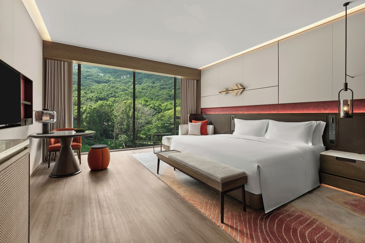 A modern hotel room with a large bed, a desk, a bench, and a TV.