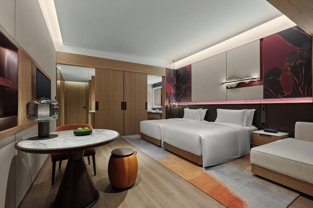 A modern hotel room with a bed, a sofa, a dining table, and a TV.