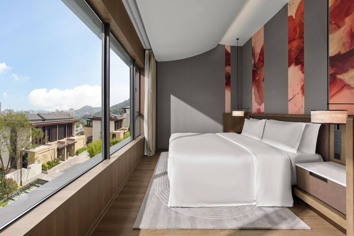 A modern bedroom with a large bed, a view of buildings, and a cityscape.