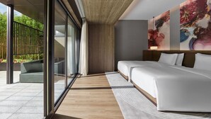 Une chambre d’hôtel moderne dotée d’un grand lit, d’un coin salon et offrant une vue sur la verdure environnante.