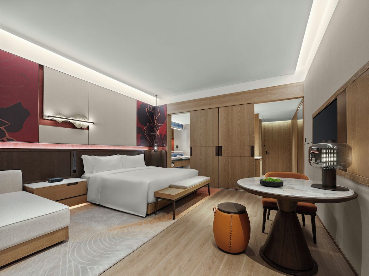 A modern hotel room with a bed, bedside tables, a desk, and a dining area.