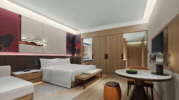 A modern hotel room with a bed, bedside tables, a desk, and a dining area.