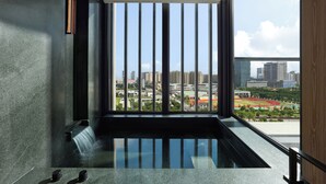 Une chambre moderne dotée d’une grande fenêtre, d’un élément décoratif intégré avec de l’eau et offrant une vue sur le paysage urbain.