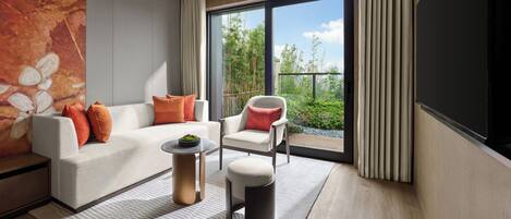 Una sala de estar moderna con un sofá, un sillón y una mesa de centro, un ventanal con vistas a zonas verdes, y un cuadro en la pared.