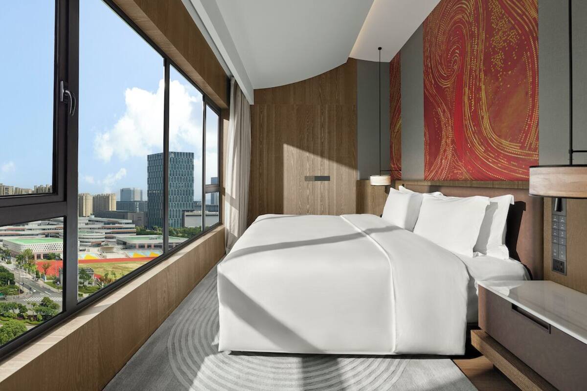 A modern hotel room with a large bed, a view of the cityscape, and a decorative wall.