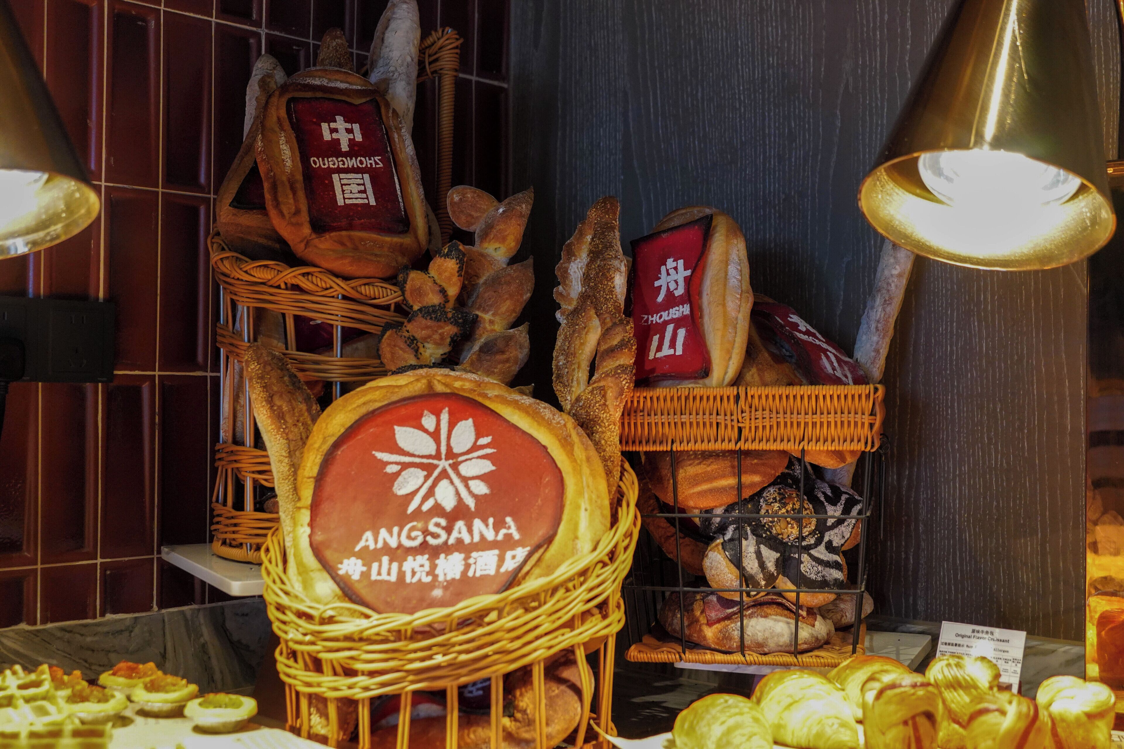 A bakery display with various breads and pastries, including a sign for Angsana.