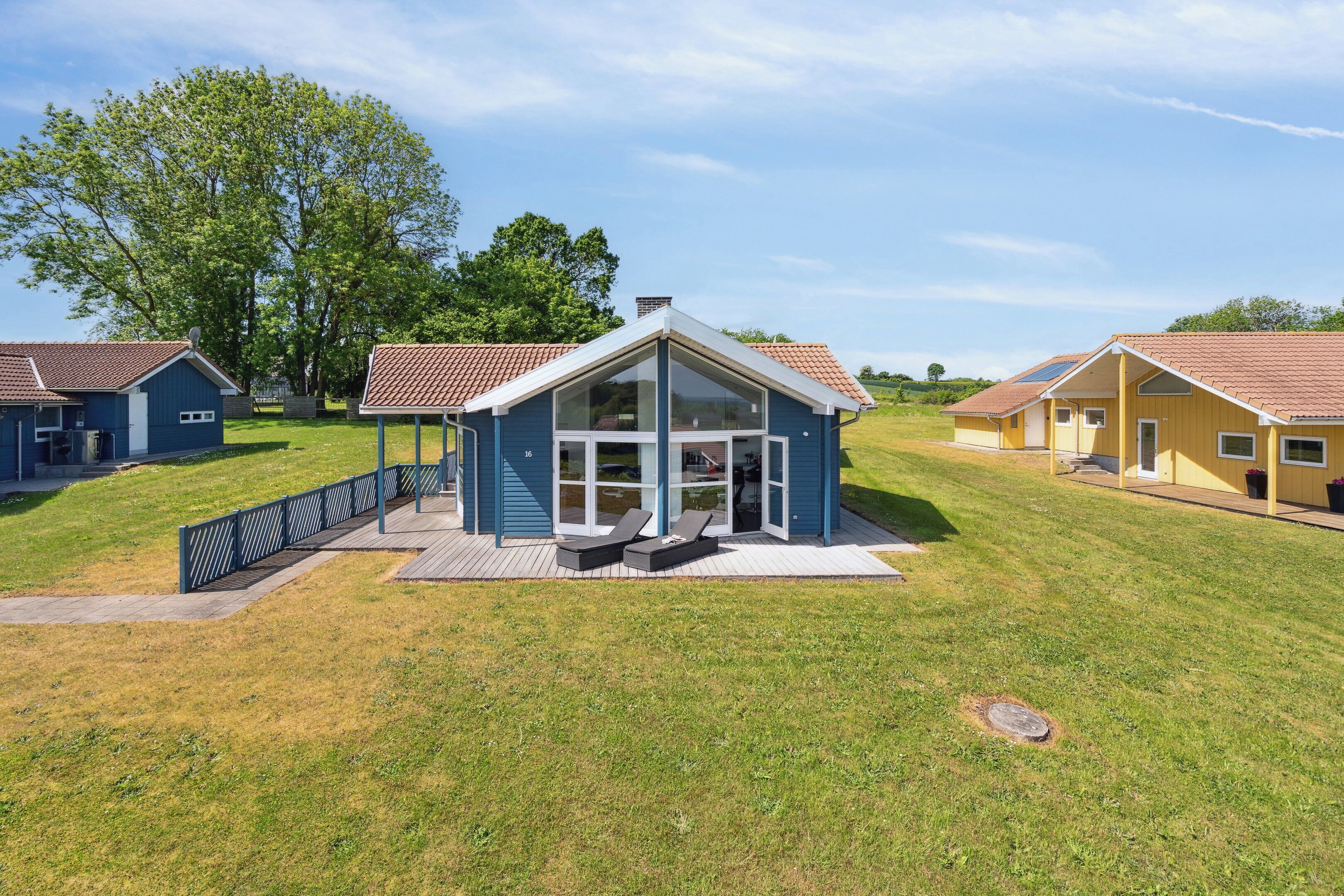 Ein modernes Haus mit Glasfront, einer Terrasse und einem kleinen Sitzbereich im Freien.
