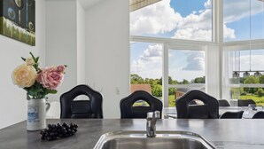 Une cuisine moderne avec un évier en acier inoxydable, un vase rempli de fleurs et une vue sur l’extérieur grâce à de grandes fenêtres.