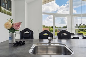 A modern kitchen with a stainless steel sink, a vase with flowers, and a view of the outdoors through large windows.