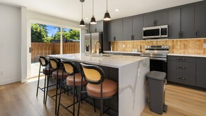 A modern kitchen with a large island, bar stools, dark cabinets, and stainless steel appliances. - Stylish Eastside 3BR Family Home Prime Location (Bellevue)