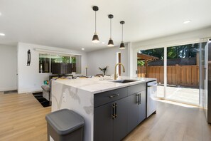 Une cuisine moderne dotée d’un grand îlot central, de meubles de couleur noire et de luminaires suspendus.