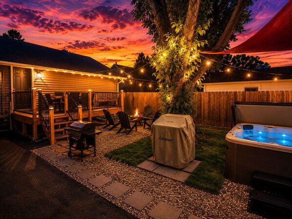 A backyard with a deck, outdoor furniture, a hot tub, and string lights.