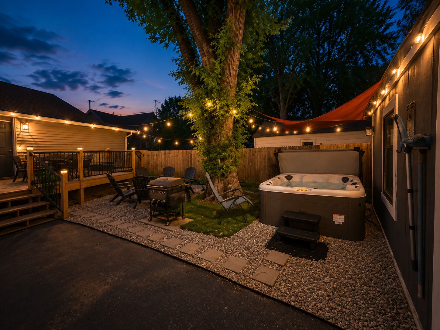 A backyard with a hot tub, string lights, a barbecue grill, and outdoor seating.