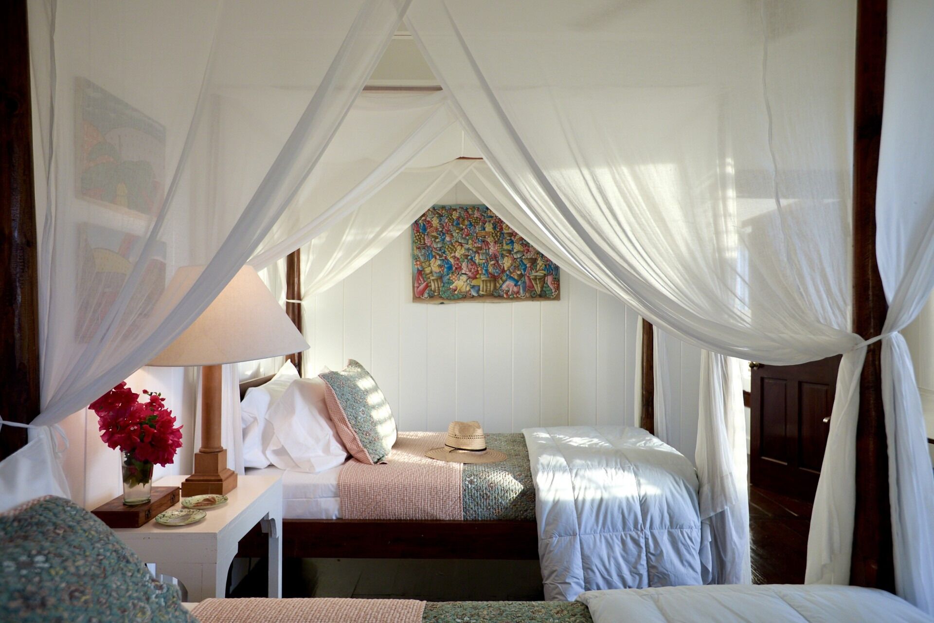 Ein Schlafzimmer mit einem Himmelsbett, einem Nachttisch mit Lampe, einer Blumenvase und einem farbenfrohen Wandteppich.