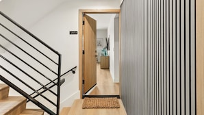 A modern interior with a wooden staircase, a sign reading "UNIT A", and a room with a striped wall and a wooden cabinet. - Tide House  | Manhattan Beach - Unit A - Seaside w/ Parking (Manhattan Beach)