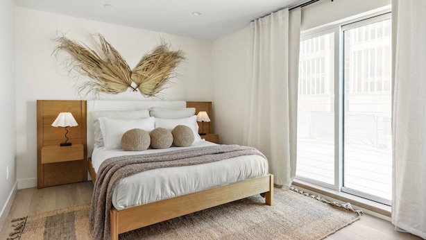A modern bedroom with a wooden bed, white bedding, and a large window with curtains. - Tide House  | Manhattan Beach - Unit A - Seaside w/ Parking (Manhattan Beach)