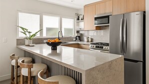 A modern kitchen with a large island, stainless steel appliances, and wooden cabinets. - Tide House | Manhattan Beach - Unit B - Seaside w/ Parking (Manhattan Beach)