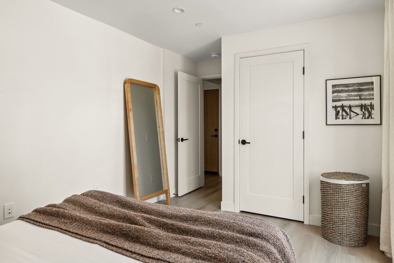 Quarto com cama, espelho, porta e um quadro na parede.