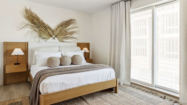 A modern bedroom with a wooden bed, white bedding, and a large window with sheer curtains. - Tide House | Manhattan Beach - Unit C - Seaside w/ Parking (Manhattan Beach)