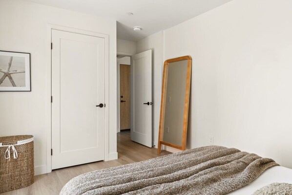 A bedroom with a bed, a wooden-framed mirror, a wicker basket, and a framed picture on the wall.
