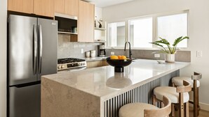 A modern kitchen with stainless steel appliances, a central island, and a window providing natural light. - Tide House | Manhattan Beach - Unit C - Seaside w/ Parking (Manhattan Beach)