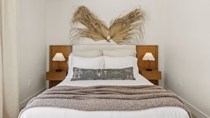 Una cama bien hecha con un cabecero decorativo, dos lámparas de noche y un plaid con textura.
