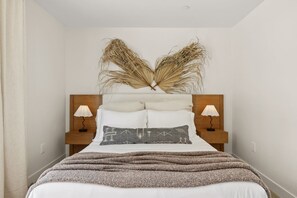 Un letto rifatto con cura, una testiera decorativa, due lampade ai lati e una coperta con trama.