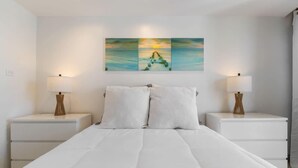 A bedroom with a large bed, two bedside tables with lamps, and a wall-mounted painting.