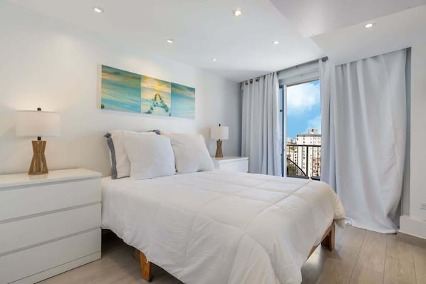 Un dormitorio moderno con una cama grande, dos mesitas de noche con lámparas, un cuadro en la pared y un balcón con cortinas.