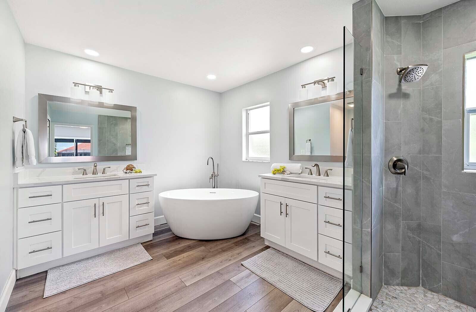 A modern bathroom with a freestanding bathtub, two sinks with mirrors, and a shower area.