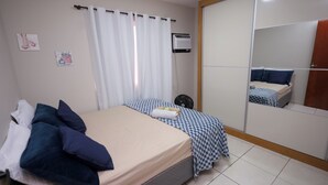 A bedroom with a bed, a bedside fan, a mirror, and a wall-mounted air conditioner.