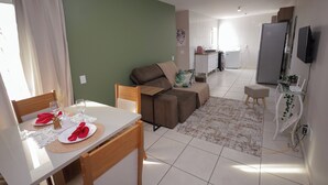 A living room with a sofa, a dining table set with plates and glasses, a TV, and a kitchen in the background.