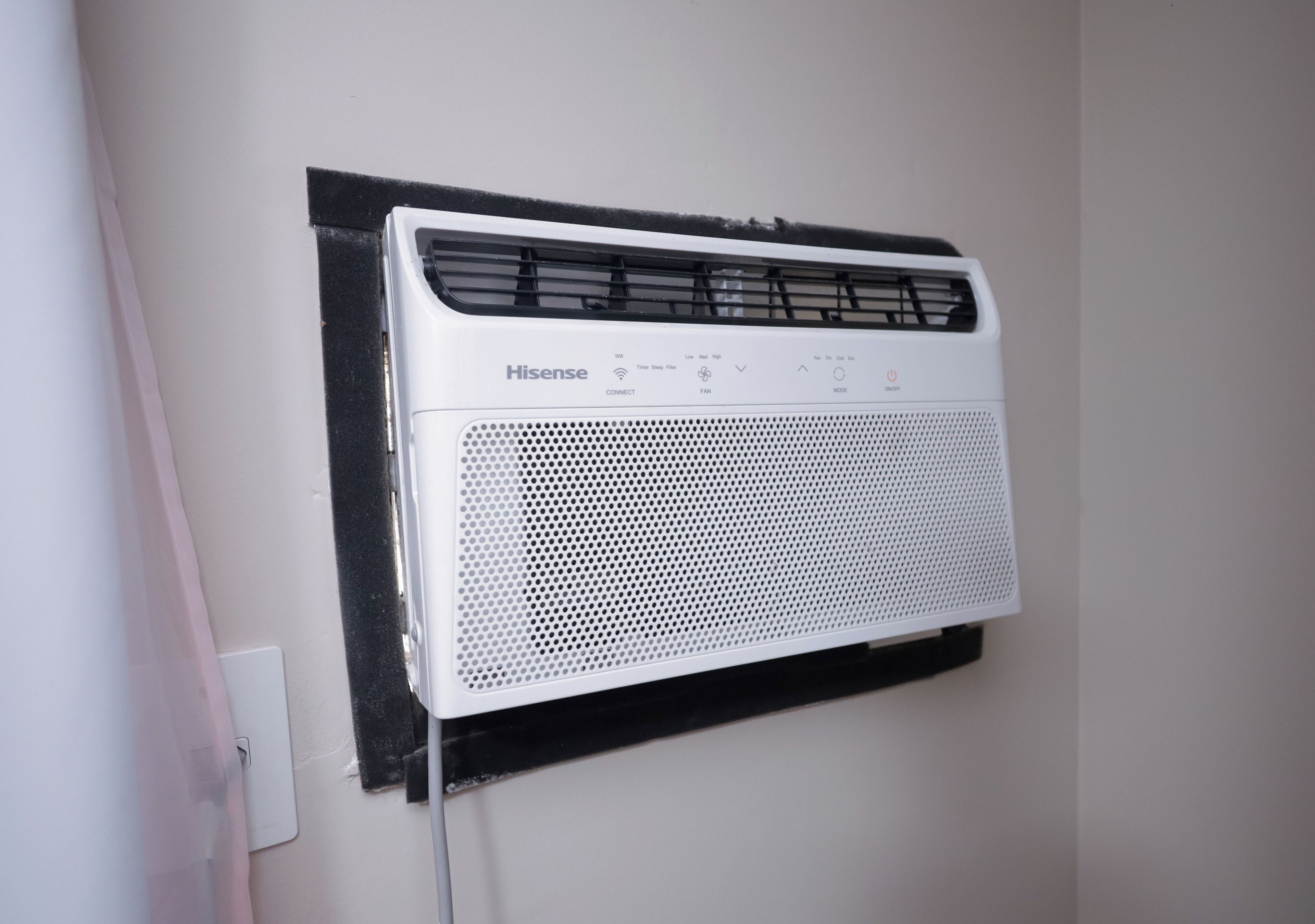 A white Hisense air conditioner mounted on a wall with a black protective cover.