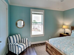 A bedroom with teal walls, a striped chair, a wooden bed, a window, and a nightstand with a lamp.