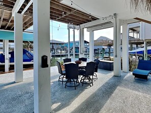 An outdoor covered patio with a table and chairs, overlooking a marina with boats and buildings.