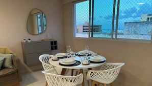 A dining area with a round table set for four, white chairs, a grey cabinet, and a large window with a view of buildings.