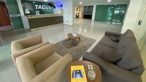 A modern lobby with a reception desk labeled "TAGUS Home & Business," a seating area with sofas and a coffee table, and a glass partition in the background.