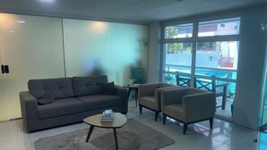 A modern living room with a grey sofa, two armchairs, a coffee table, and a large window offering a view of the outside.