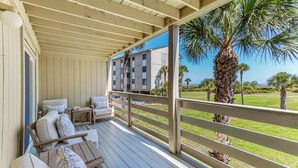 A covered outdoor seating area with wooden furniture, a view of a building, and palm trees.