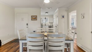 Un comedor con mesa y sillas, un ventilador de techo y vista a la cocina.