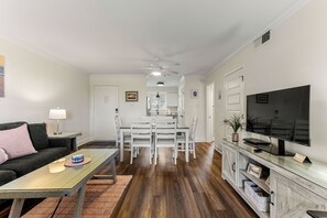 Un salon comprenant un canapé, une table basse, un téléviseur, un coin repas avec des chaises et un ventilateur de plafond.