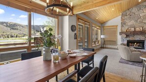 Zona pranzo con tavolo in legno, sedie, un vaso con fiori e vista sull'esterno.